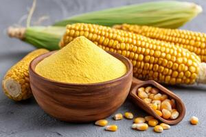 Corn flour in bowl with fresh corn cobs and kernels on grey table photo