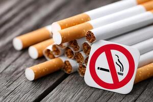 No smoking sign leaning on pile of cigarettes on rustic wood table photo