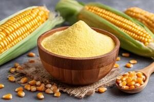 Corn flour in wooden bowl with fresh corn cobs on grey table photo