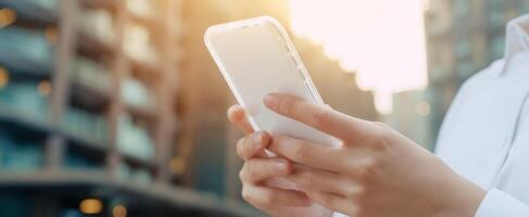 The smartphone held in hands against a modern urban backdrop during sunset. photo