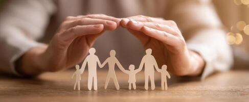 The hands protecting a family of paper figures in a warm setting. photo