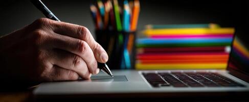 The pen glides across a laptop in a colorful creative workspace. photo