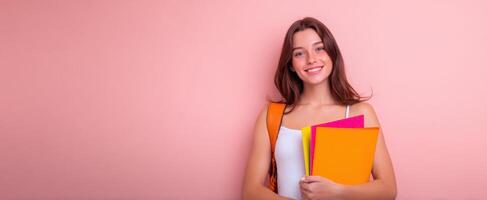 The cheerful student holding colorful folders against a pink background. photo