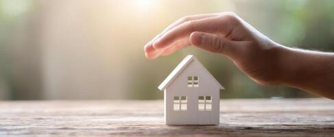 The hand protecting a miniature house on a wooden table. photo