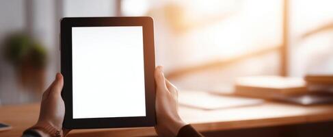 The hands holding a blank tablet in a bright modern workspace setting. photo
