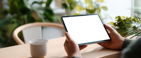 The tablet in hands surrounded by greenery and warm coffee in a cozy space. photo