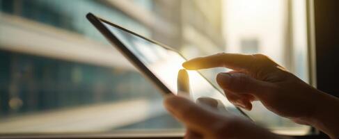 The person using a tablet near a window with urban sunlight illuminating surroundings. photo