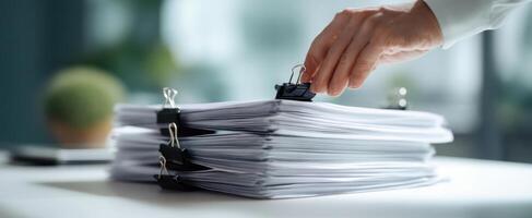 The hand organizing a stack of documents with binder clips on a desk. photo