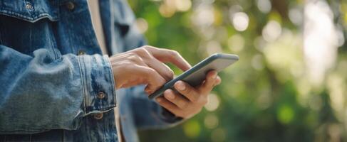 The person using a smartphone in a lush green outdoor setting. photo
