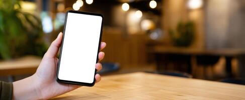 The smartphone in a hand with a blank screen in a cozy cafe setting. photo
