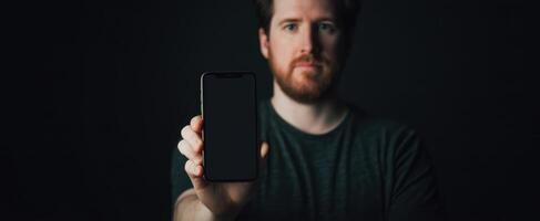The man holding a smartphone in a dark, minimalist setting. photo