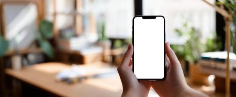 The smartphone held in hands with a blank screen in a modern workspace photo