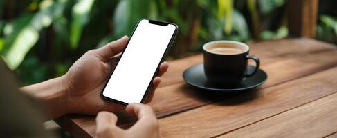 The smartphone resting beside a cup of coffee on a wooden table. photo