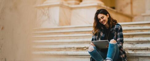 The woman enjoying her tablet while sitting on outdoor staircase steps. photo