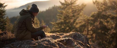 The person enjoying technology while sitting on a rock in nature. photo