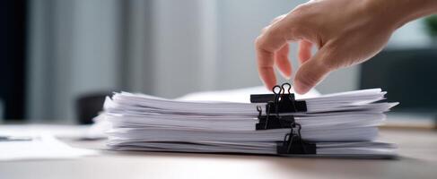 The hand organizing paperwork with binder clips on a modern desk setup. photo