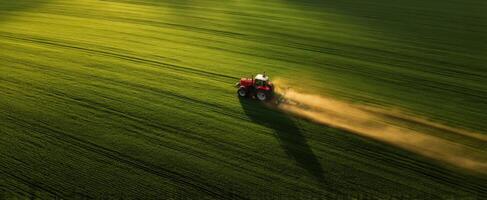 The tractor plowing a vibrant green field at sunset with dust trails. photo