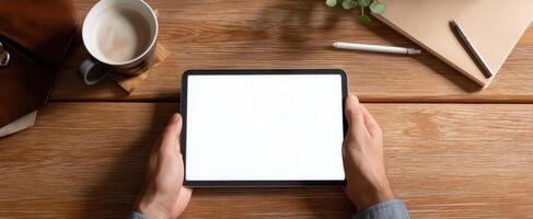 The tablet resting in hands against a rustic wooden workspace backdrop. photo