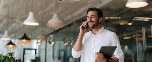 The smiling man using a smartphone and tablet in a modern office setting. photo