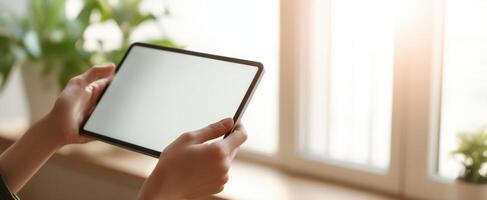 The tablet held in hands against a sunlit window with plants. photo