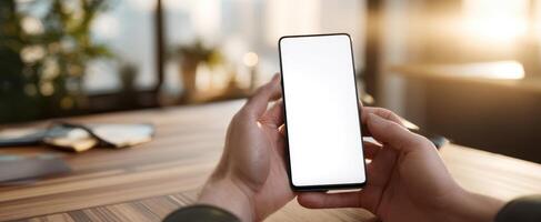 The smartphone held in hands with a blank screen in a modern workspace. photo