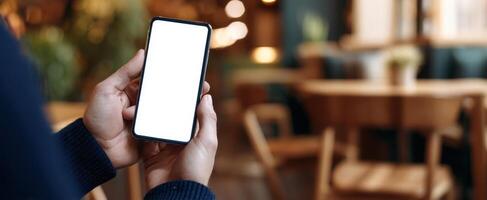 The smartphone held in a hand showing a blank screen in a cozy cafe setting photo