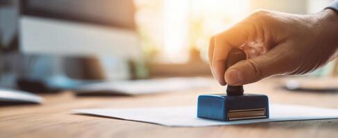 The hand pressing a blue stamp on official paperwork in an office setting. photo