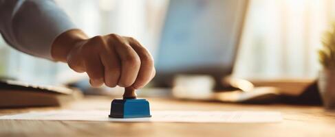 The hand using a blue stamp on important paperwork in a modern office setting. photo