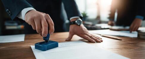 The businessman applying a stamp to official documents on a wooden desk. photo