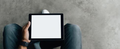 The tablet held by a person sitting on a minimalistic floor environment. photo
