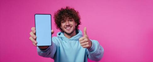 The cheerful young man showcasing a smartphone against a vibrant pink background. photo