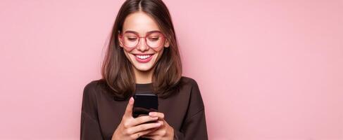 The smiling woman using her smartphone against a pink backdrop. photo