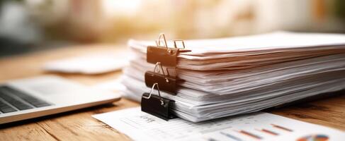 The stack of organized paperwork beside a laptop in a modern office. photo