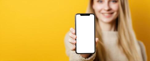 The smiling woman holding a smartphone with a blank screen on a yellow background photo