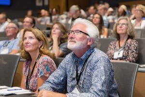 Attendees Engaged in Corporate Conference with Audience Watching Speaker Stage Presentation photo
