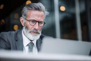 Mature Businessman Wearing Eyeglasses and Suit Working on Laptop with Concentration photo