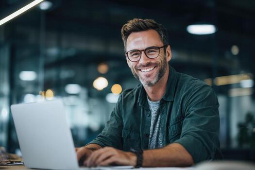 Professional Man Smiling While Working on a Laptop in an Office photo