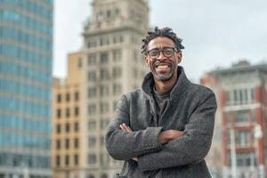 Man with glasses wearing a jacket standing in front of city buildings photo