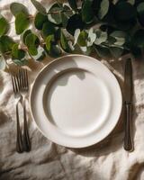 An Empty Plate with Silverware and Greenery on Tablecloth Background Stock photo