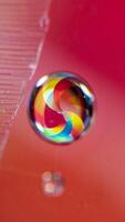 Vibrant Rainbow Swirl in Water Droplet on Red Surface Macro Photography photo
