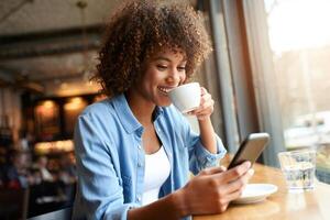 Coffee Background Young Woman with Curly Hair Enjoying Coffee and Smartphone in Cafe photo