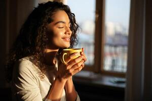 Coffee Background Serene Young Woman with Curly Hair Enjoying a Warm Drink by Window photo