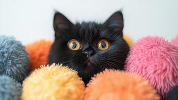 A black cat with yellow eyes peeking out from a pile of colorful pom poms photo