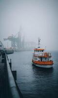 Mystical harbor scene with a vibrant orange boat disappearing into the ethereal fog laden cityscape photo