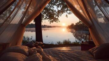 Lake view from a romantic camping tent during sunrise with cozy bed and draped sheer fabrics photo