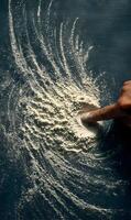 Finger traces playful patterns in flour dust creating whimsical and airy designs against a dark surface photo