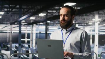 Computer scientists on data center industrial platform analyzing performance outputs on laptop. Server farm IT experts collaborating on finetuning rigs configurations, camera B video