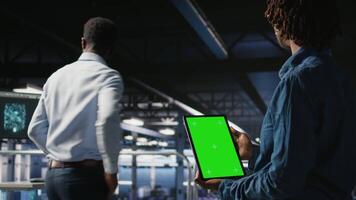 Data center engineers monitoring neural network LLM visualization using green screen tablet. Server farm IT experts oversee rigs powering machine learning processes using chroma key device, camera A video