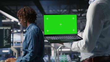 Close up of data center admins on industrial platform using green screen laptop, collaborating on tasks. Server hub workers visualizing large language model architecture using chroma key notebook video