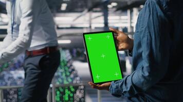 Data center engineers monitoring neural network LLM visualization using green screen tablet. Server farm IT experts oversee rigs powering machine learning processes using chroma key device, camera B video